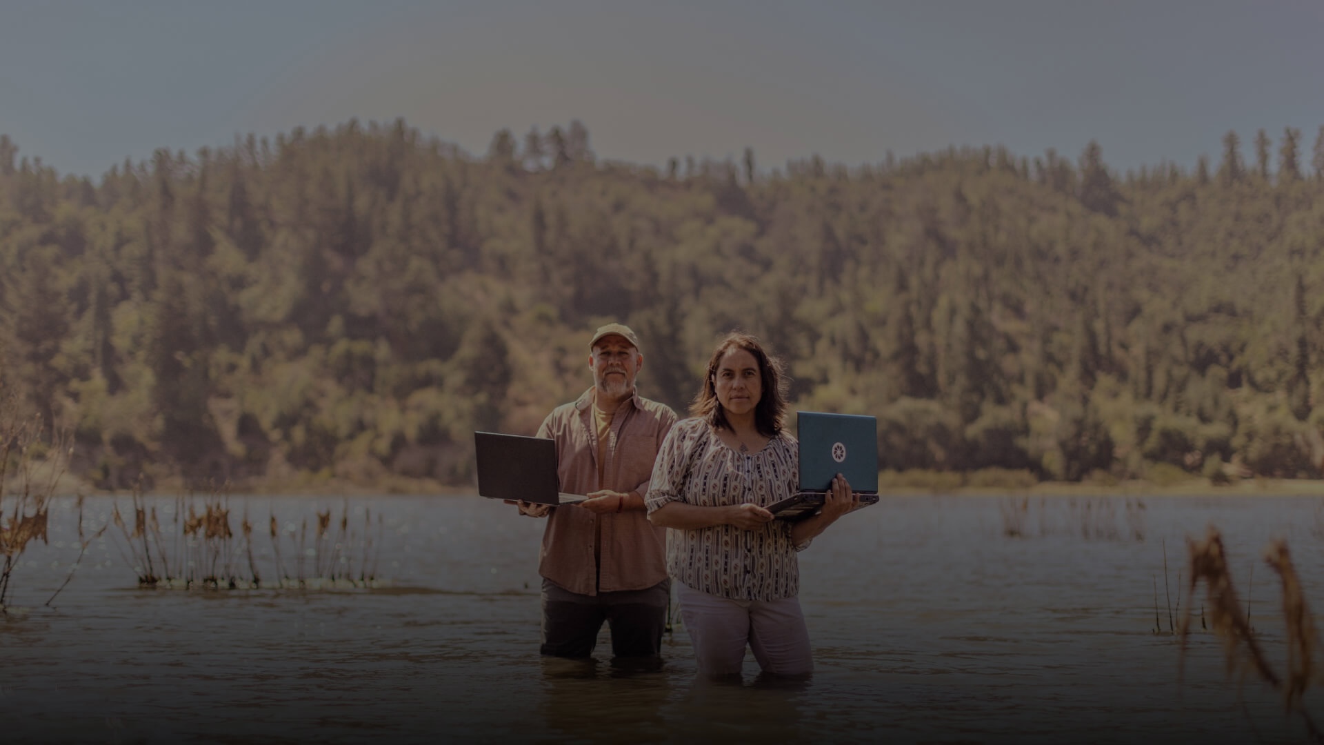 A man and woman in a marsh holding laptops